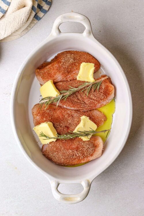 Succulent seasoned chicken breasts with butter, herbs, and spices for baking.