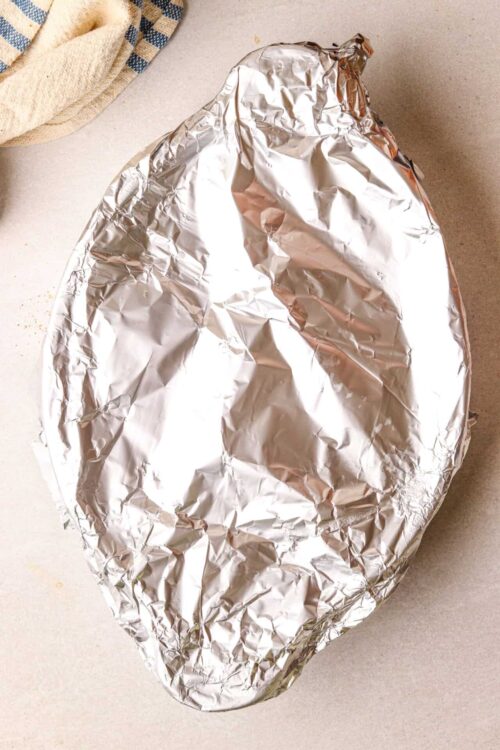 Aluminum foil wrapped roast or baked dish on countertop.