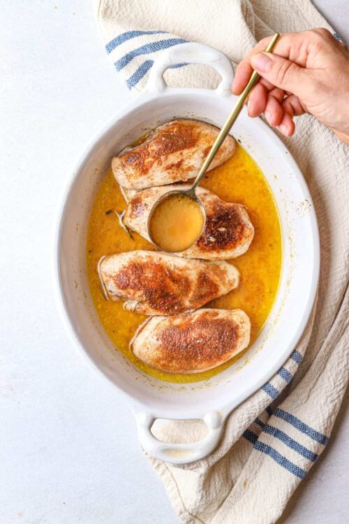 Succulent baked chicken breasts cooking in a creamy lemon butter sauce.