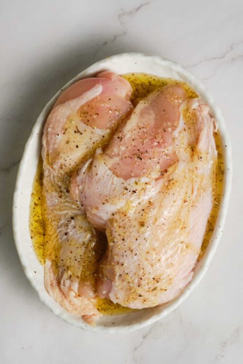 Raw chicken breasts marinated with olive oil and spices in an oval dish.