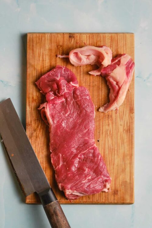 Butchered beef cut on wooden cutting board with a cleaver.