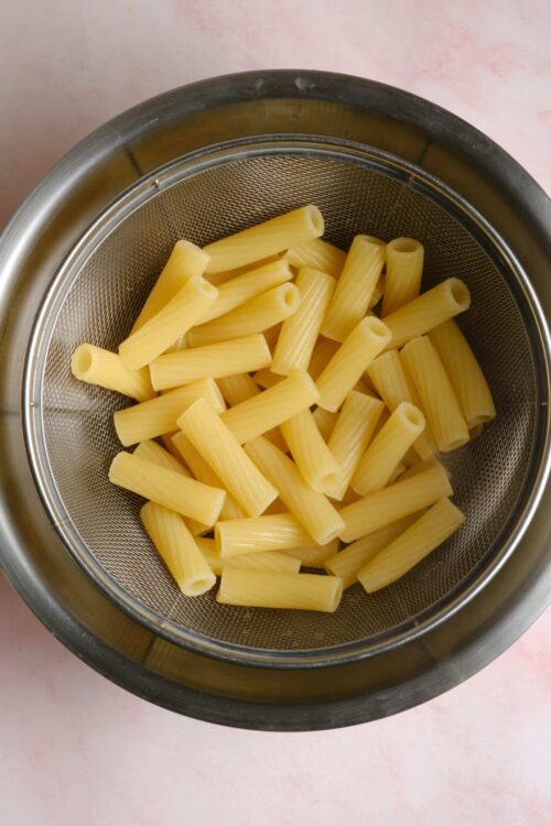 Uncooked rigatoni pasta in a stainless steel strainer.