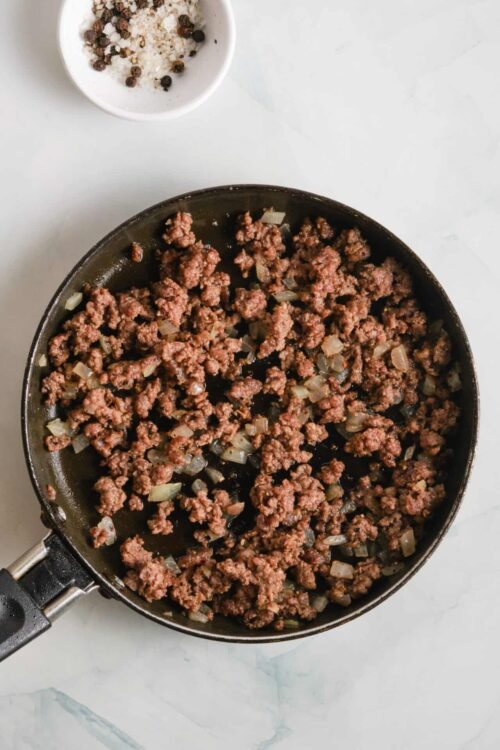 Sautéed ground beef with onions in a black skillet on white surface.