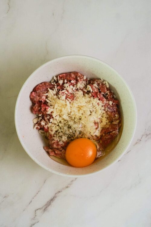 Minced meat mixture in a white bowl with an egg, ready for cooking or baking.
