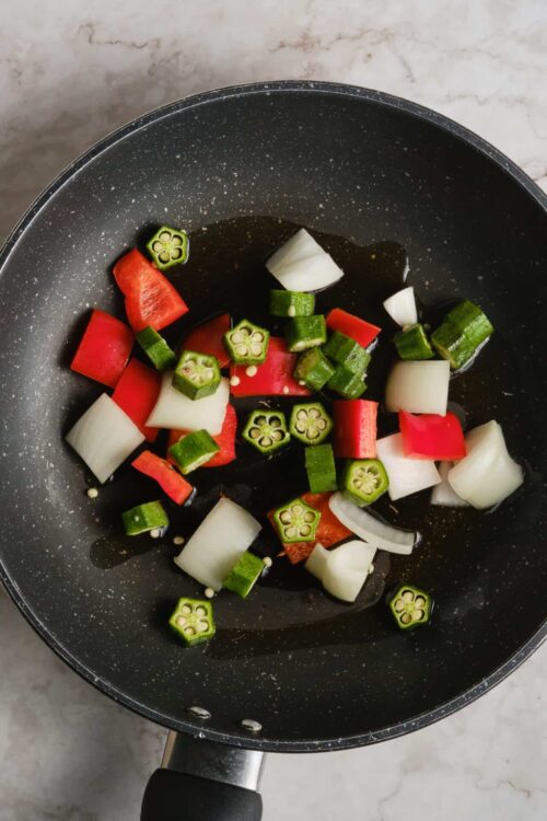 Sautéed vegetables in a black skillet with okra, watermelon radish, and onion pieces.