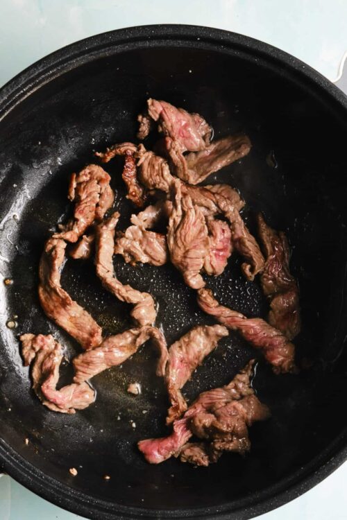 Sliced beef cooking in a black skillet for recipe preparation.
