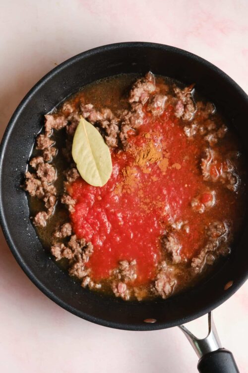 Minced beef cooking with tomato sauce in a black skillet on a pink surface.