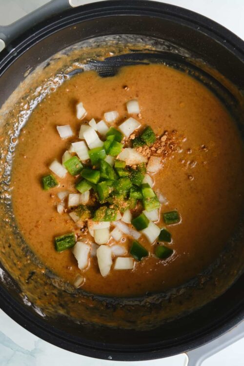 Savory soup in a slow cooker with chopped onions and green onions on top.