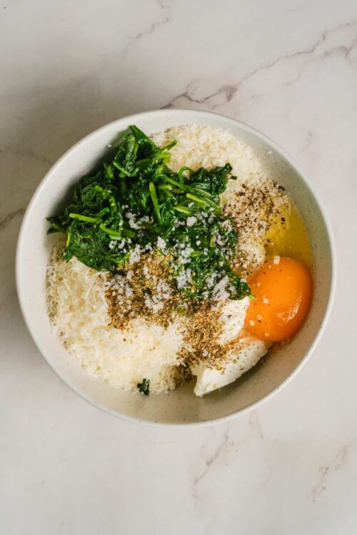Fresh spinach, grated cheese, eggs, and seasonings in a mixing bowl for healthy breakfast or cooking ingredients.