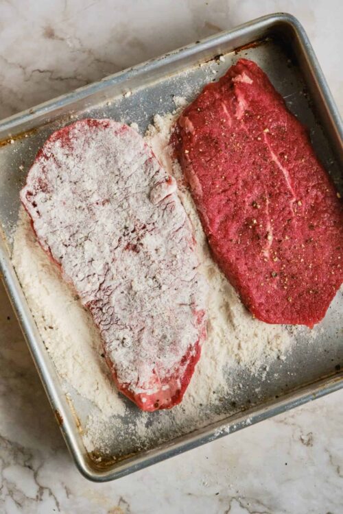 Juicy raw steaks seasoned with salt and pepper on a baking sheet.