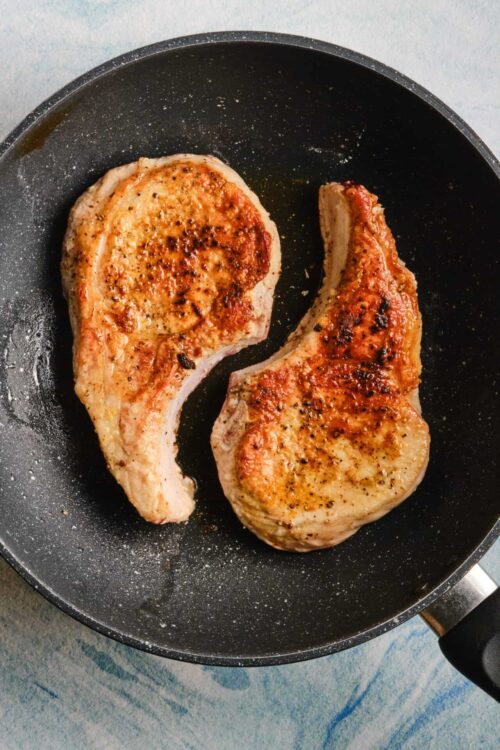 Juicy, seasoned pork chops cooking in a non-stick skillet. Perfect for easy dinner recipes with flavorful, crispy crust.
