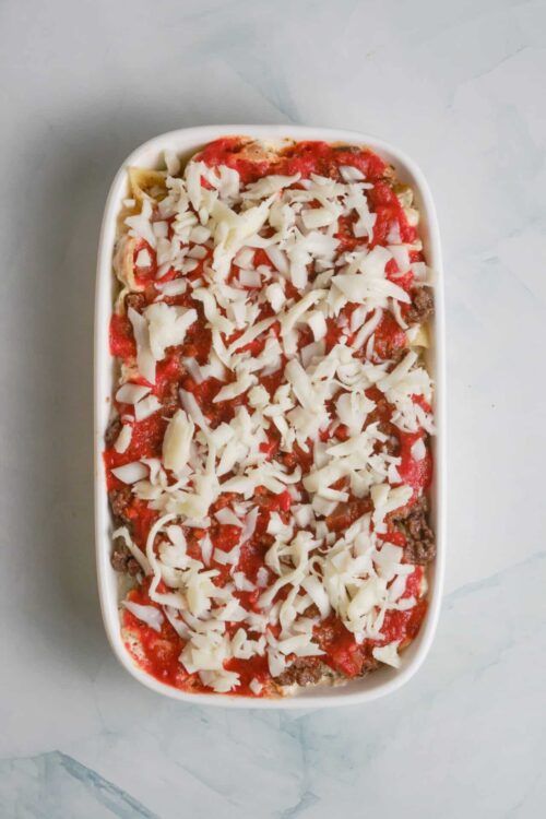 Baked ziti casserole topped with cheese and tomato sauce, ready to bake.