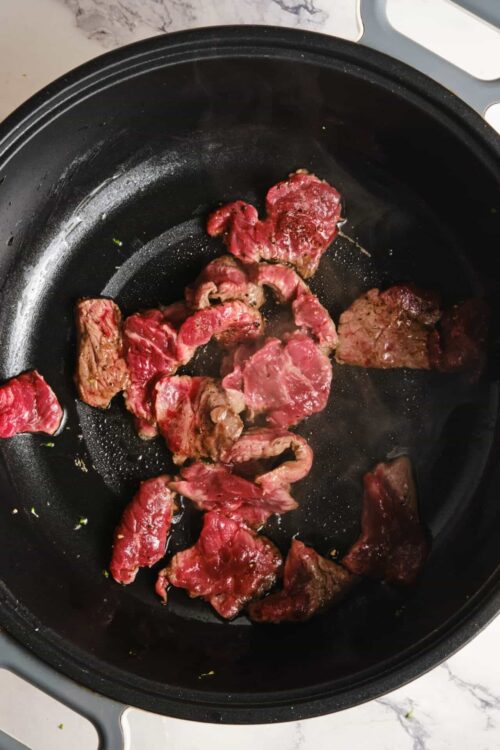Searing beef strips in an air fryer basket for roasting or stir-fry.