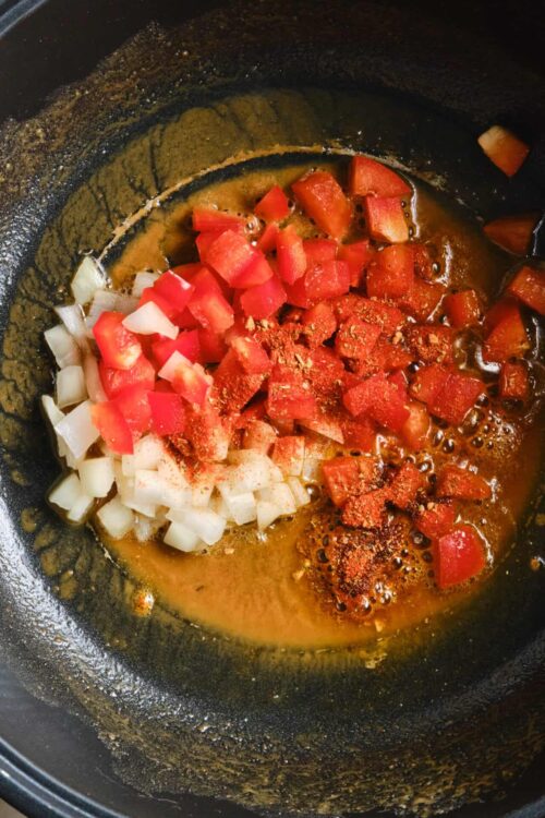 Diced onions and tomatoes cooking in a skillet with spices, preparing a flavorful dish.