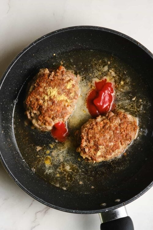 Juicy homemade beef meatballs cooking in a skillet with tomato sauce and olive oil.