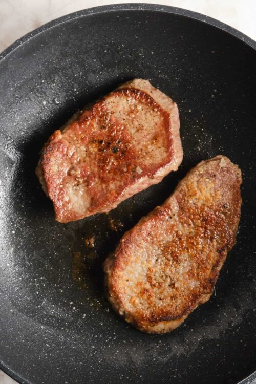 Seared beef steaks cooking in a black skillet.