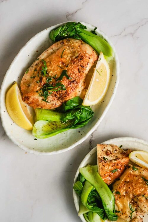 Baked salmon with lemon and greens in a white dish.