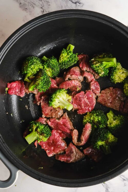 Sliced beef and broccoli cooking in a black skillet, fresh ingredients for healthy stir-fry.