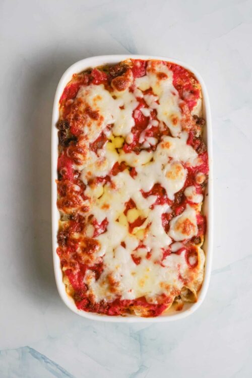 Creamy baked ziti pasta with melted cheese and marinara sauce in a white dish.