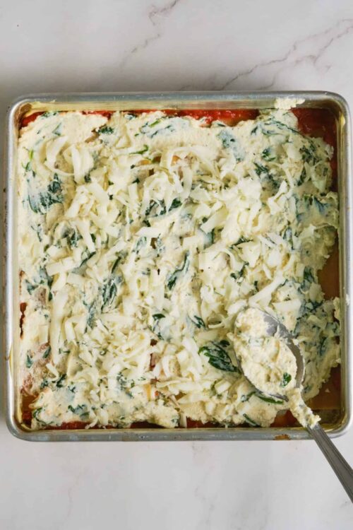 Cheesebaked spinach lasagna in a baking dish with melted cheese and spinach leaves.