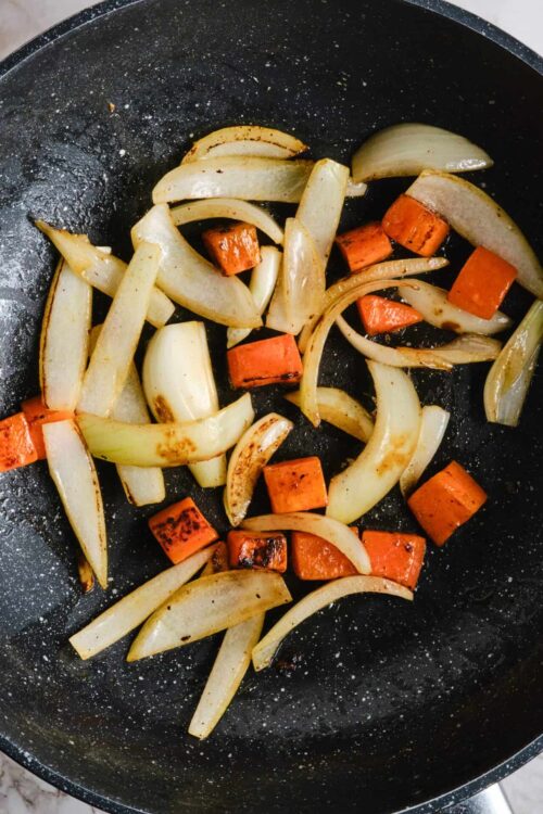 Sauteed onions and carrots in a non-stick skillet for a caramelized vegetable dish.