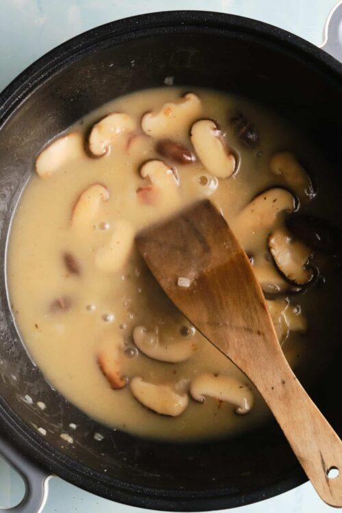 Creamy mushroom sauce cooking in a skillet with a wooden spoon. Perfect for pasta or steak dishes.