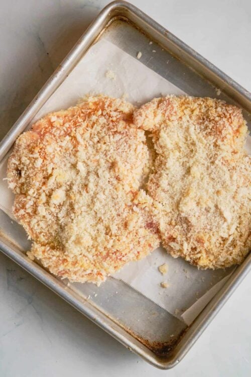Crispy baked breaded chicken breasts on a metal baking sheet with parchment paper, ready to serve.