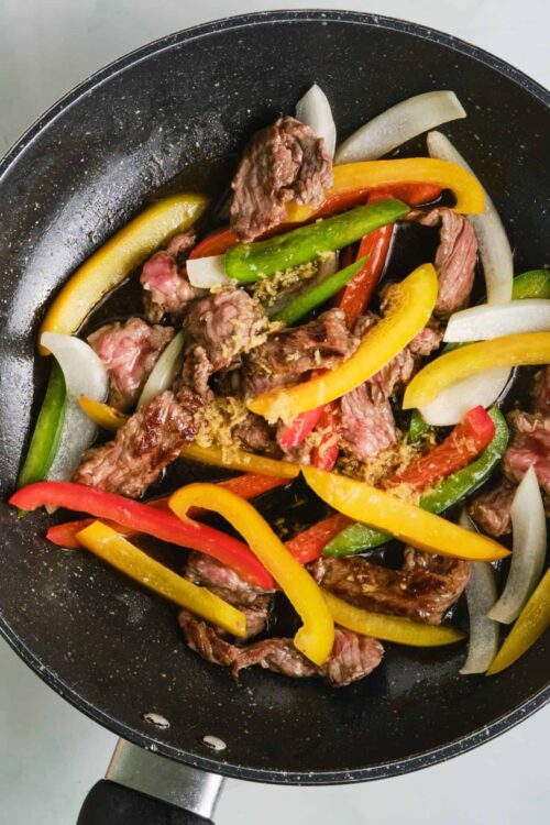 Sliced beef stir-fry with colorful bell peppers and onions in a frying pan.