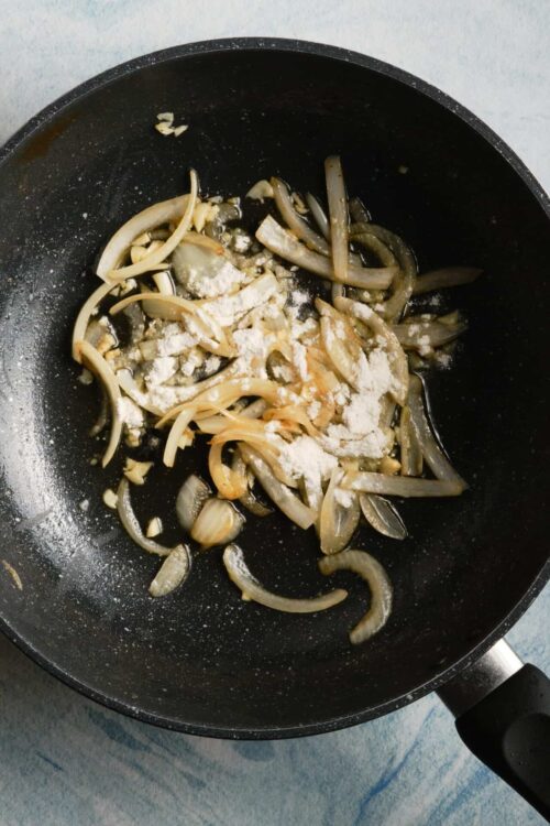 Sautéed onions and garlic cooking in a black skillet for a recipe.