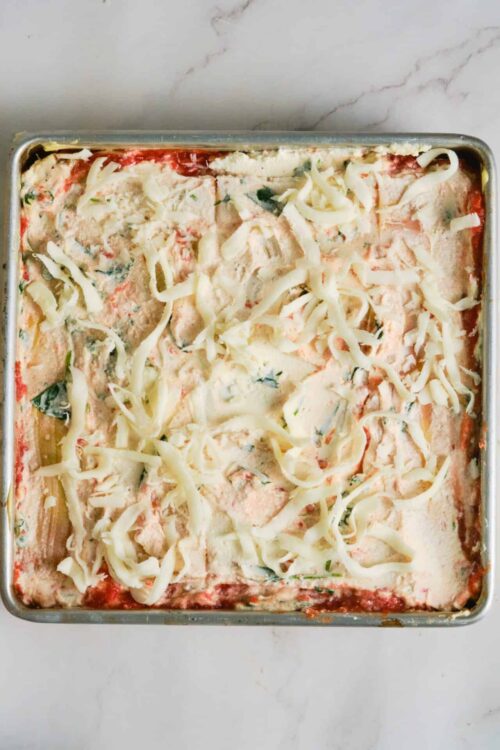 Cheesy baked lasagna with creamy sauce and melting cheese in a rectangular baking dish.