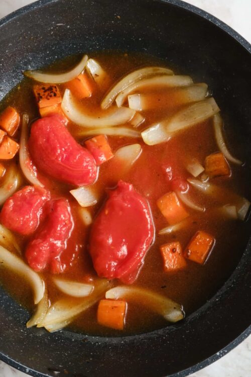Broth with tomatoes, onions, carrots, and spices in a skillet for hearty soup or stew.