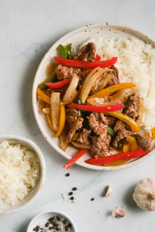 Succulent beef and bell pepper stir-fry served with white rice on a white plate.