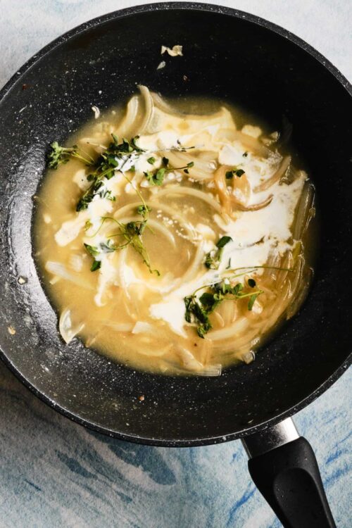 Creamy onion and thyme sauce cooking in a non-stick skillet.