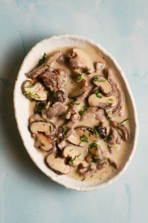 Creamy mushroom and beef stroganoff in an oval serving dish, garnished with fresh herbs.