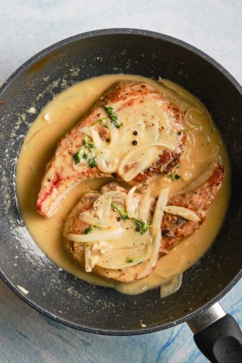 Juicy skillet chicken breasts in a creamy onion sauce, garnished with fresh herbs. Perfect for a flavorful dinner recipe.