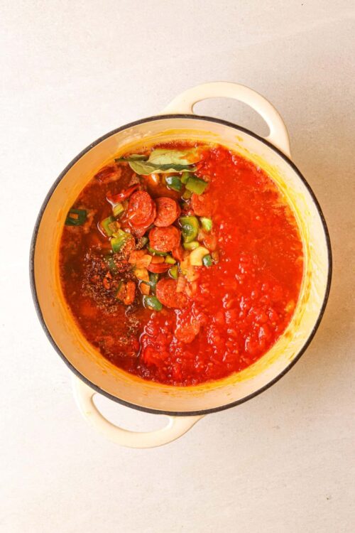 Savory homemade sausage and tomato soup in a pot on a neutral background.