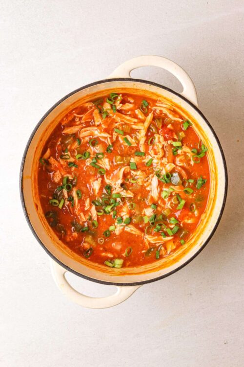 Creamy chicken and vegetable tortilla soup in a white enameled cast iron pot, garnished with chopped green onions.