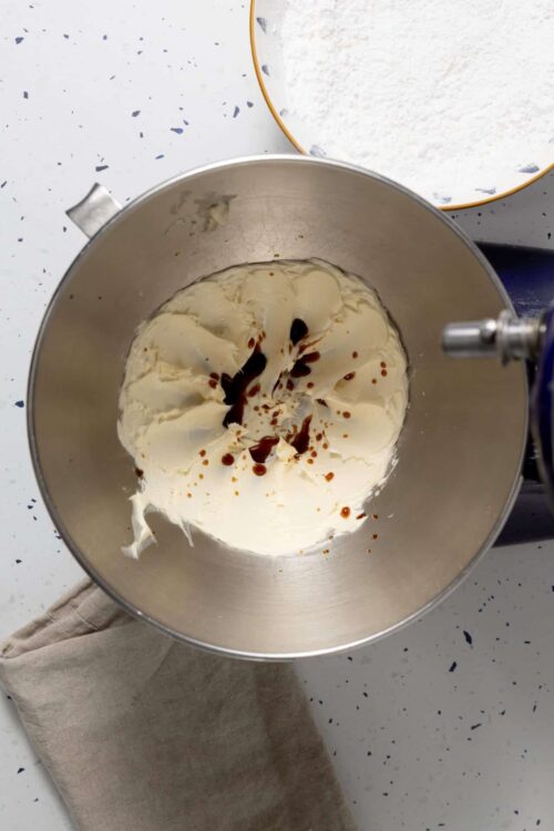 Cream cheese and vanilla bean mixture in a stand mixer bowl for baking recipes.