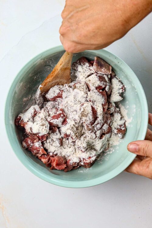 Diced meat and flour mixture in pastel green bowl for baking recipe.