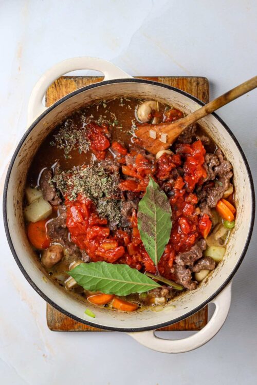 Hearty beef stew with vegetables and fresh herbs in a white enamel pot.