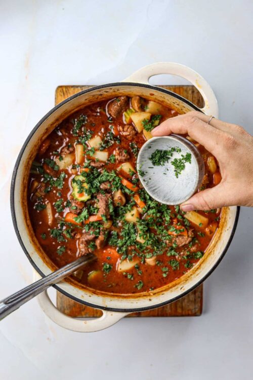 Hearty beef stew with potatoes, carrots, and herbs in a white enamel pot.