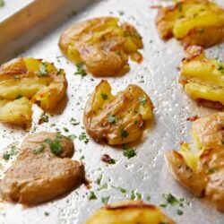 Golden roasted potatoes with herbs on baking sheet.