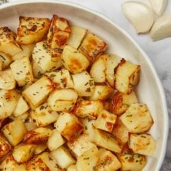 Crispy roasted garlic potatoes with fresh herbs in a white baking dish.
