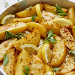 Golden roasted lemon chicken with fresh herbs and lemon wedges in a baking dish.
