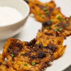 Grilled chicken skewers with smoky marinade, served with a creamy dipping sauce on a white plate.