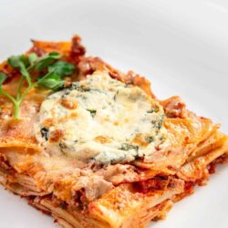 Baked lasagna with cheese and herbs on white plate.