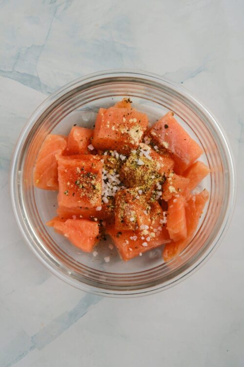 Fresh cubed watermelon with salt, pepper, and seasoning for a flavorful fruit snack.