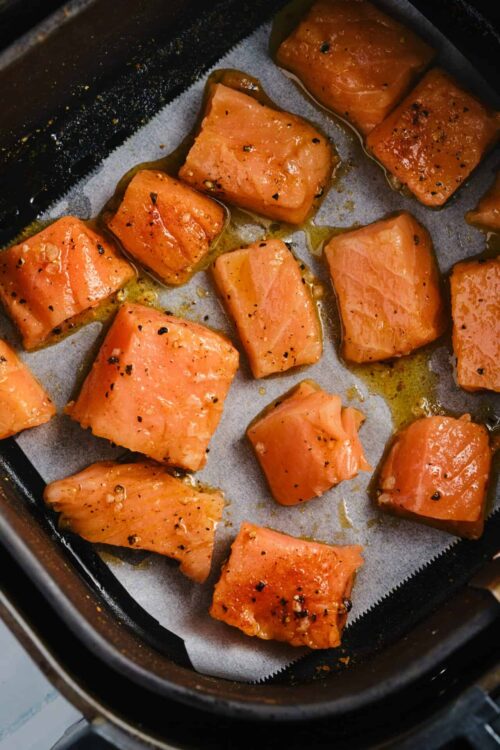 Salmon fillets cooking in air fryer with black pepper and seasoning.
