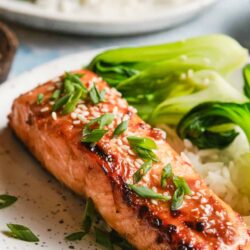 Salmon with scallions and sesame seeds on a white plate.