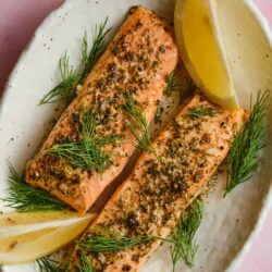 Baked salmon with herbs and lemon on a white platter, fresh dill garnish for healthy seafood recipe.